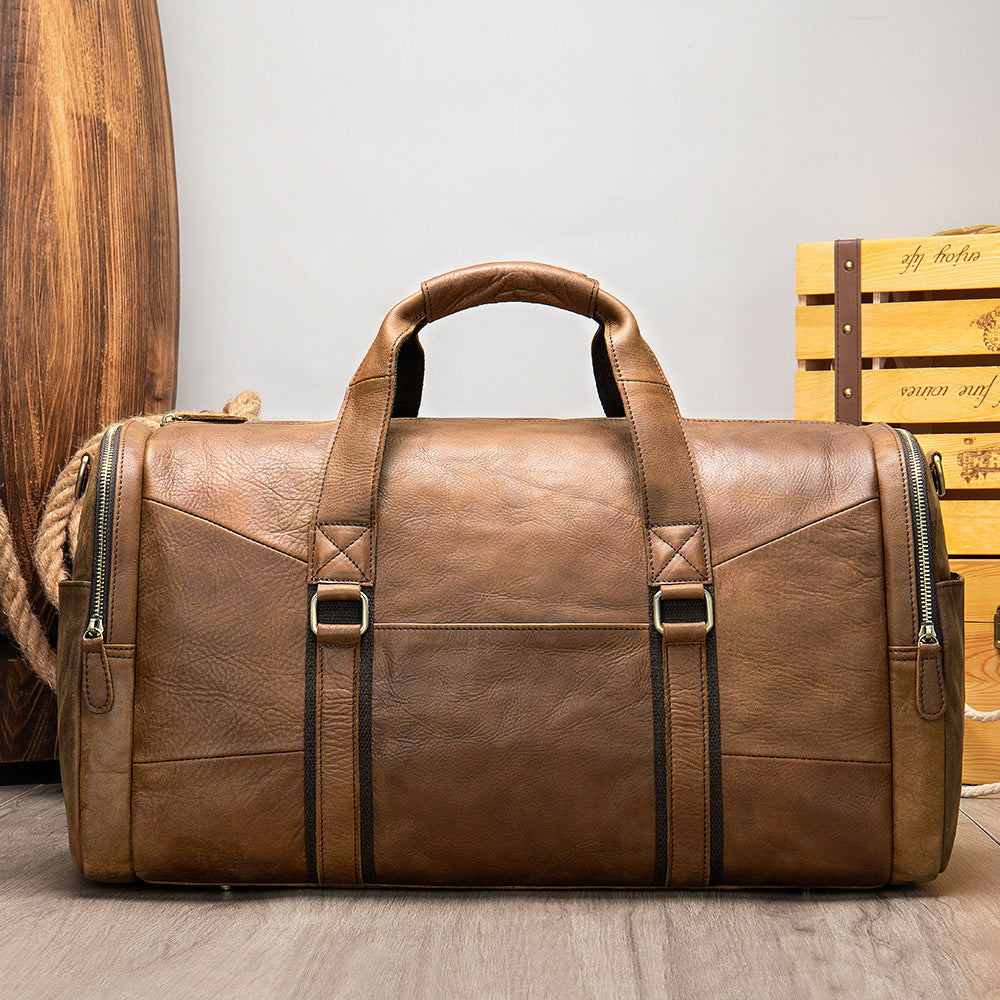 Brown leather duffel bag with zippers on a wooden floor.