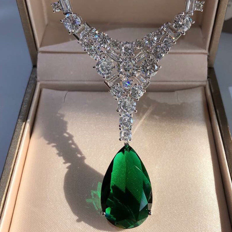 Elegant diamond necklace with a green teardrop pendant in a jewelry box.