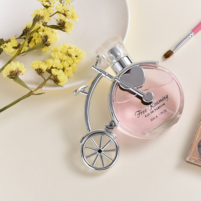 Perfume bottle with bicycle design on a light background with yellow flowers