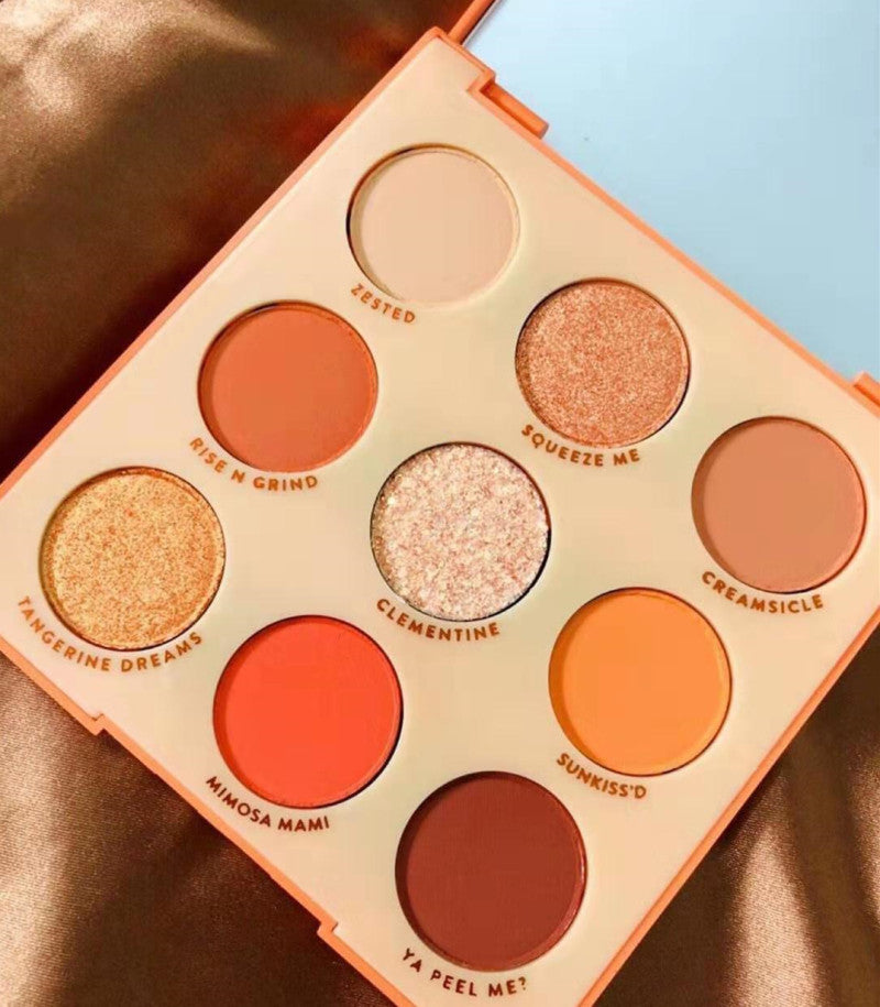 Makeup palette with various shades of orange and pink on a gold surface