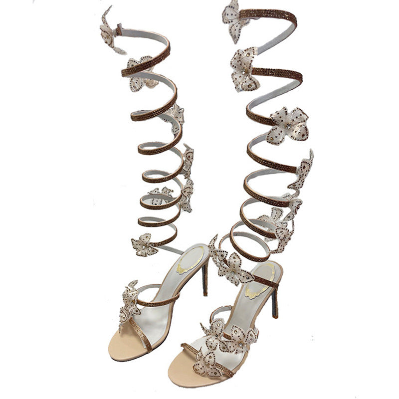 Pair of high-heeled sandals with spiral straps and decorative elements on a white background