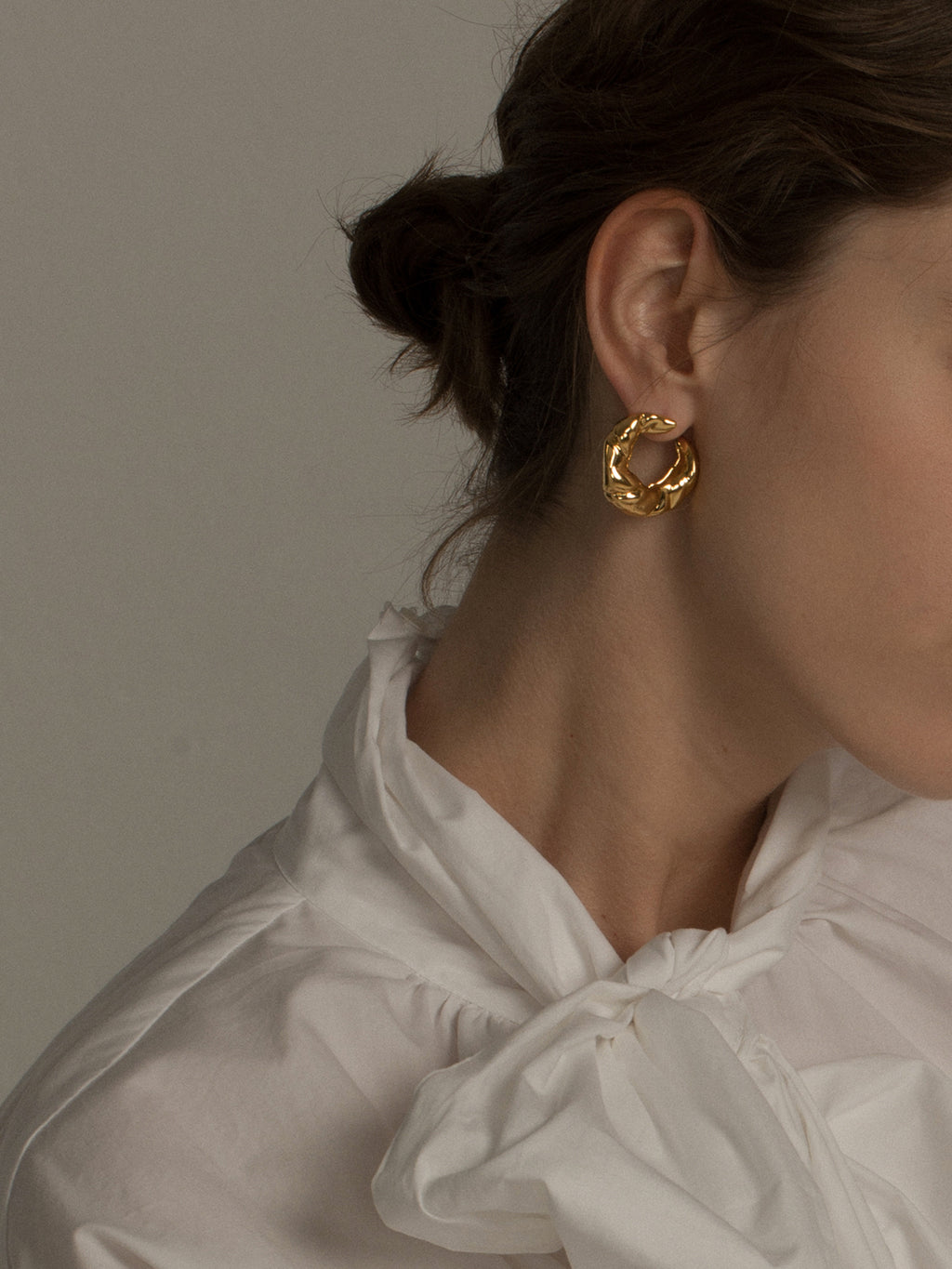 Close-up of a person wearing gold hoop earrings with a neutral background