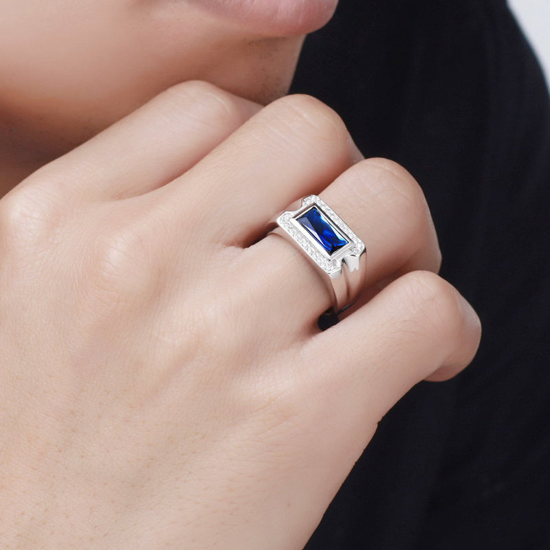 Silver ring with a blue gemstone on a person's finger against a blurred background