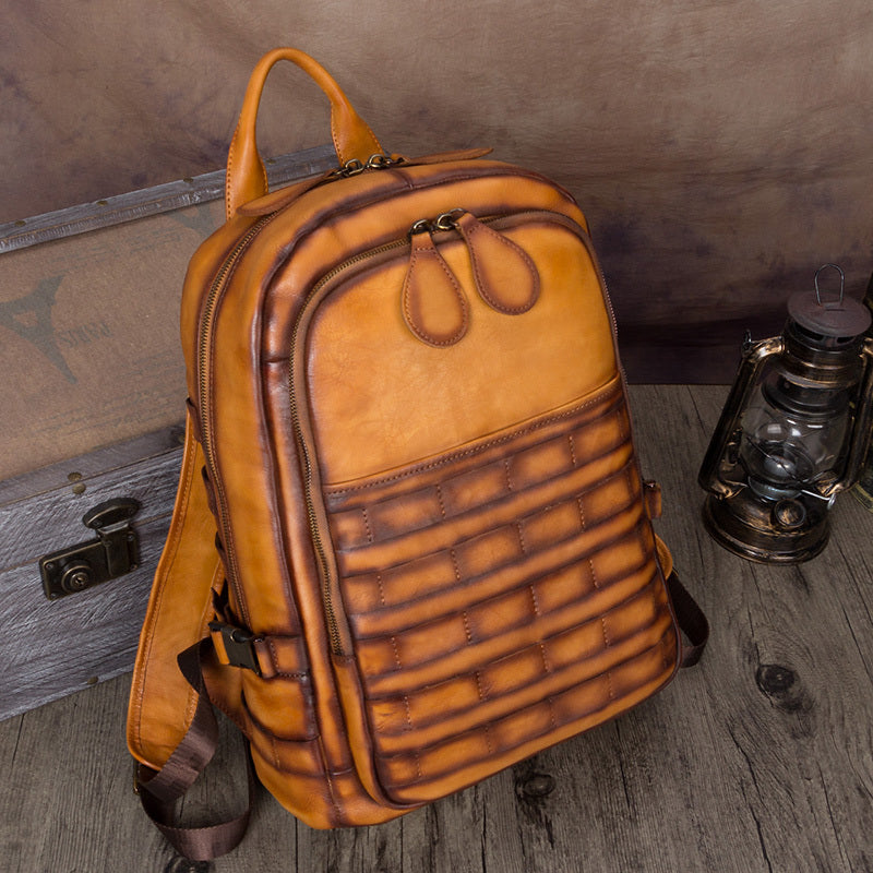 Brown leather backpack on a wooden surface with a suitcase and lantern in the background