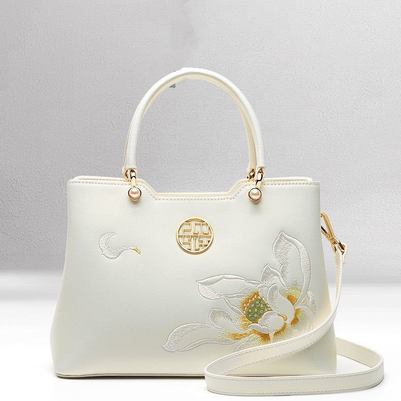White handbag with floral embroidery and gold accents on a light gray background