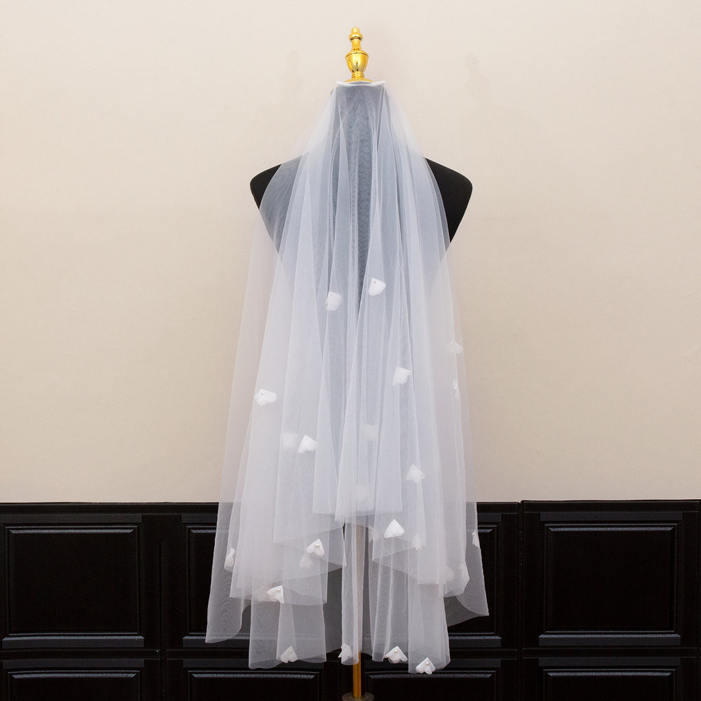 White tulle veil with heart-shaped cutouts on a mannequin against a beige wall.