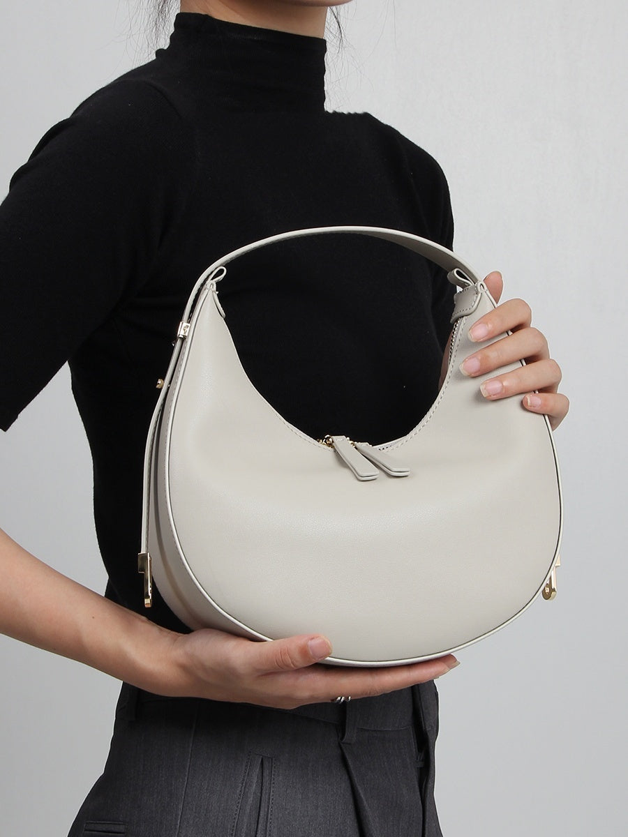 Person holding a light gray handbag against a plain background