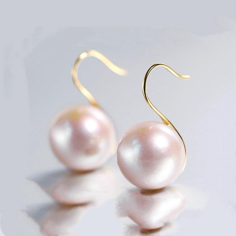 Pearl earrings with gold hooks on a reflective surface