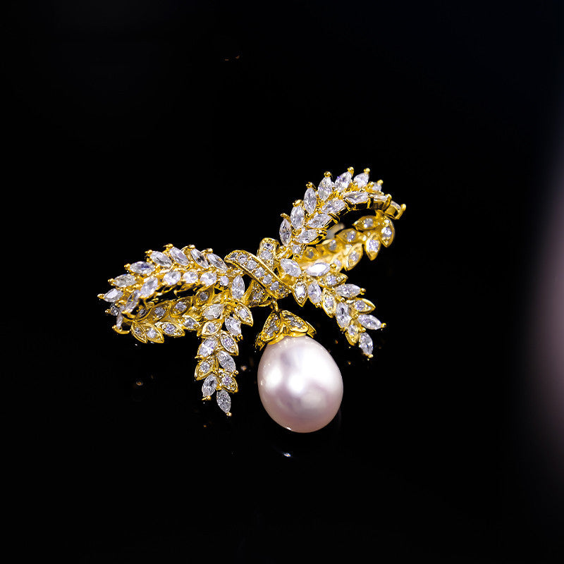 Gold bow-shaped brooch with a pearl on a black background