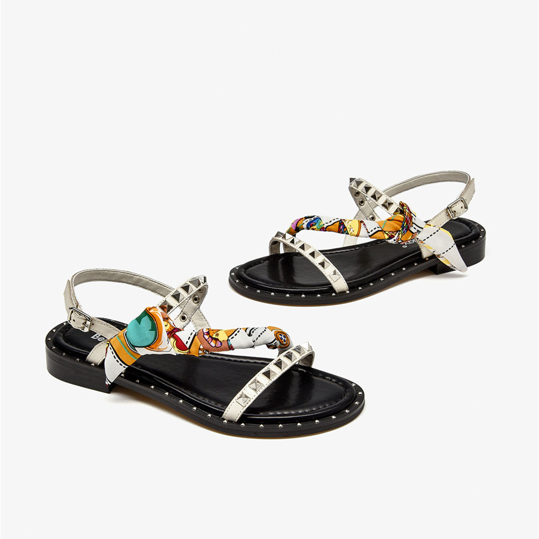 Pair of black sandals with colorful straps and silver studs on a white background