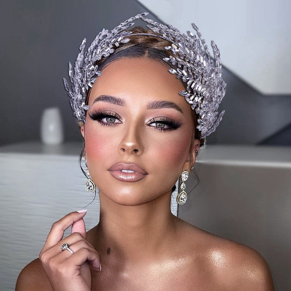 Woman wearing a sparkling silver tiara and earrings against a neutral background