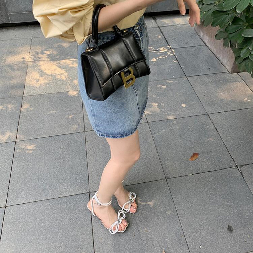 Person wearing a black handbag with a gold logo on a tiled pavement.