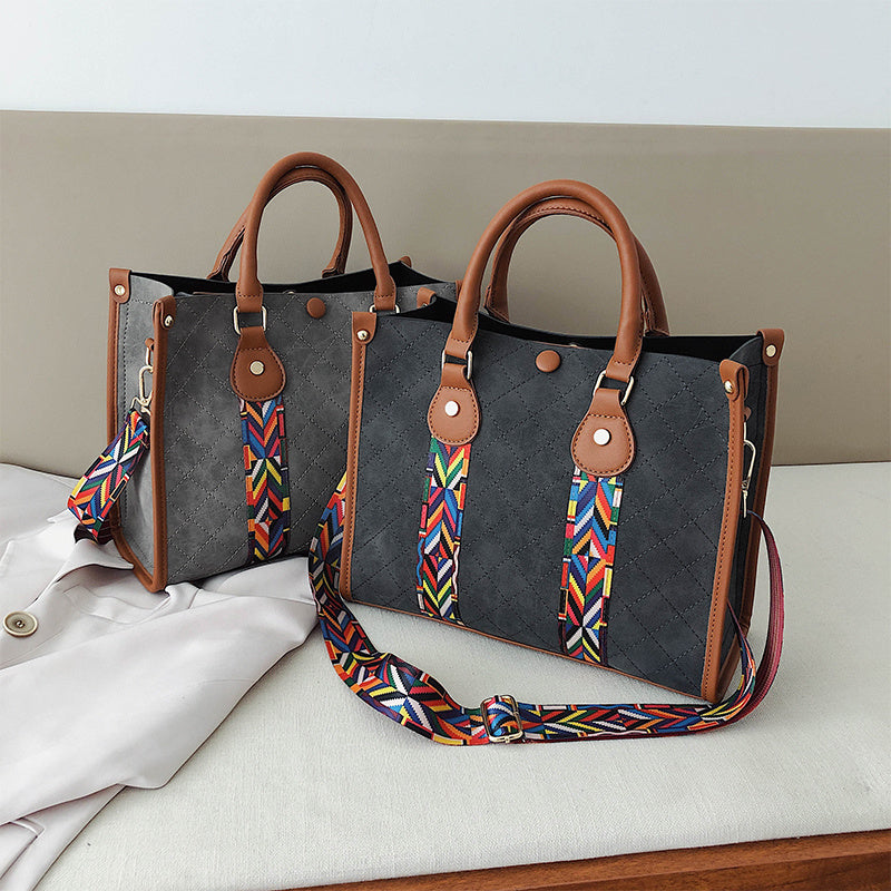 Gray handbag with brown handles and a colorful strap on a white surface.