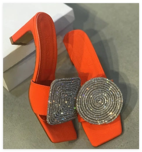 Orange high-heeled shoes with decorative embellishments on a reflective surface