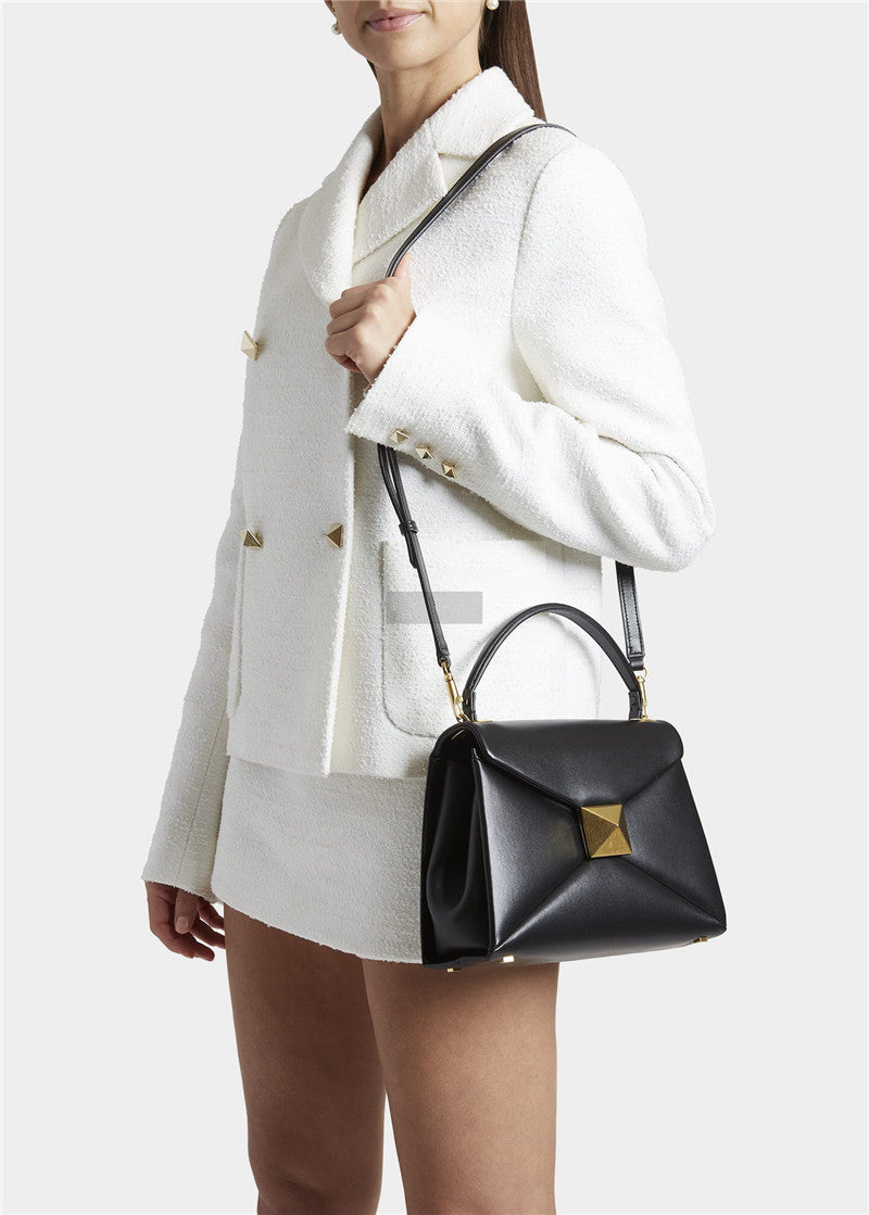 Person wearing a white coat holding a black handbag with gold accents on a light gray background