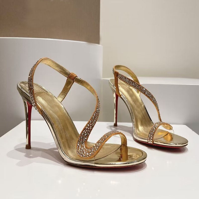 Gold high-heeled sandals with rhinestone details on a white platform.