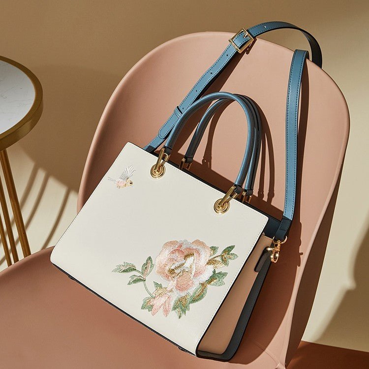 White handbag with floral embroidery and blue straps on a pink chair