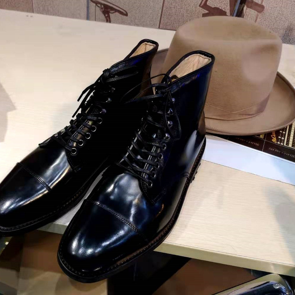 Pair of black leather shoes on a table with a beige hat in the background