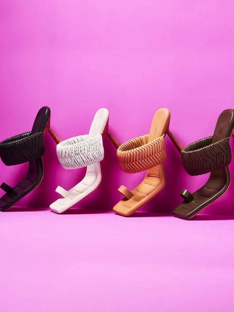 Four pairs of high-heeled shoes in black, white, orange, and brown on a pink background