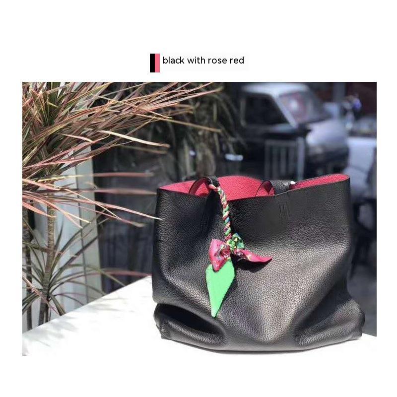 Black handbag with rose red accents and a green leaf charm on a blurred street background.