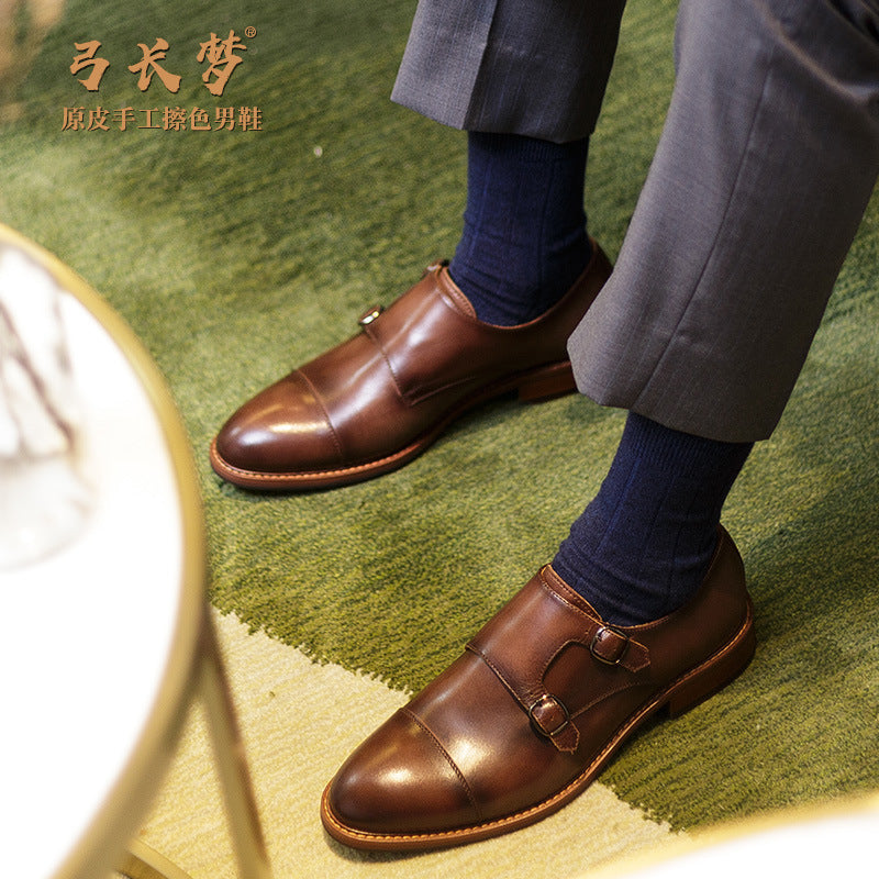 Brown leather shoes worn with a gray suit and navy socks on a green carpet.
