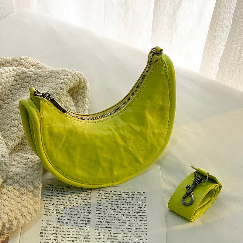 Green banana-shaped bag on a white surface with a book underneath