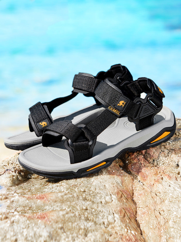 Black and gray sandals with orange accents on a rock by a blue sky.