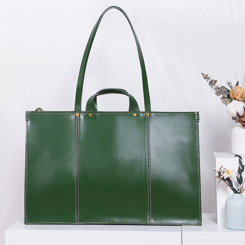 Green leather tote bag on a white surface with a minimal background