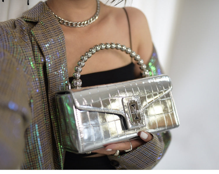 Silver handbag held by a person wearing a sparkly outfit.