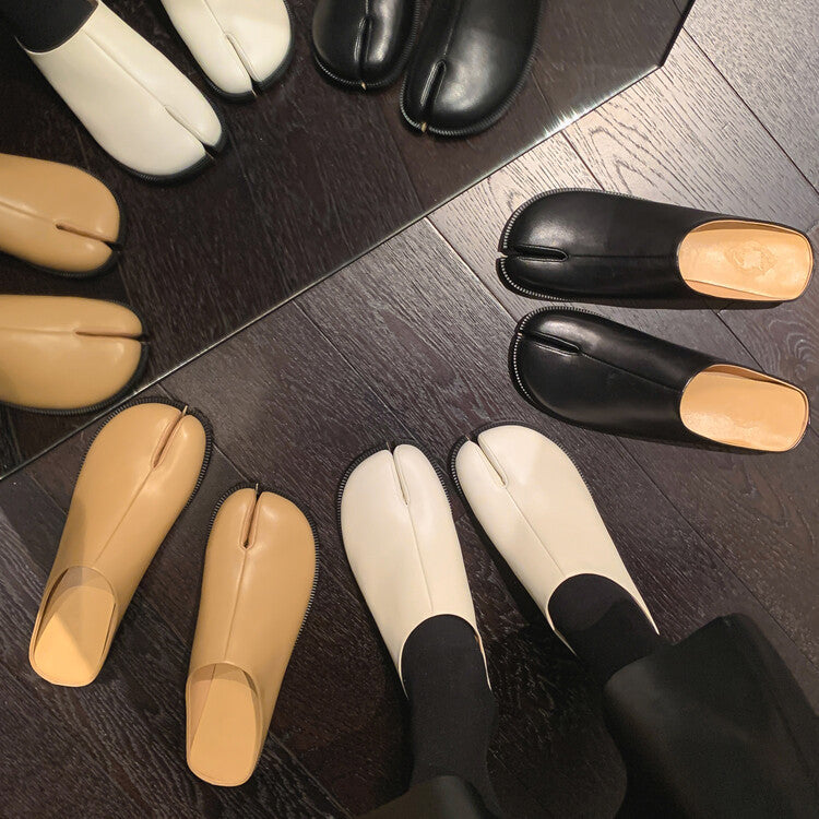 Pair of black and beige tabi shoes on a wooden floor.