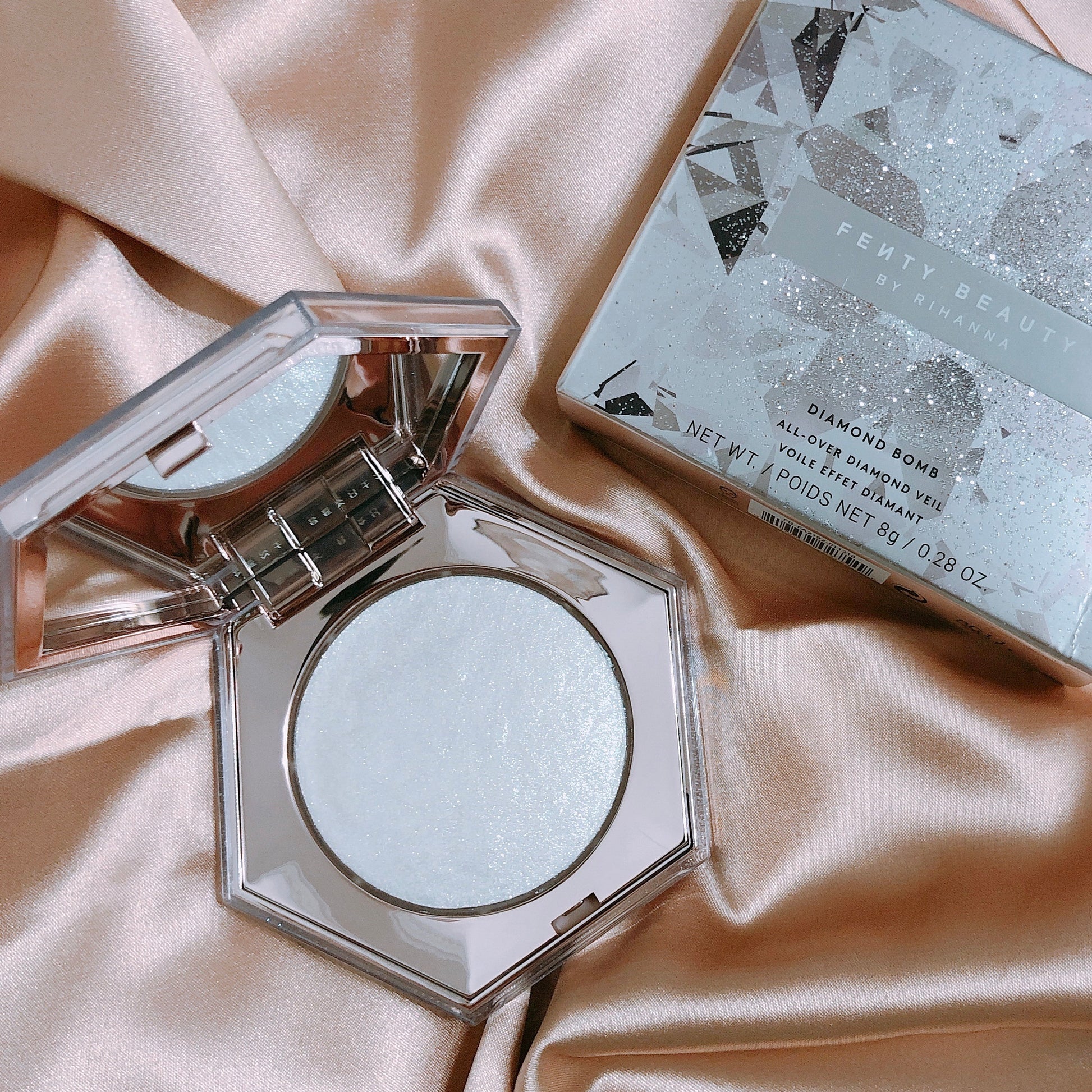 Compact powder with mirror and packaging on a satin surface