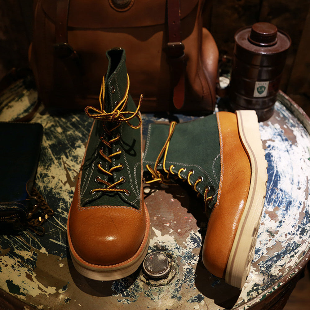 Pair of green and brown leather boots on a textured surface with a bag and bottle in the background.