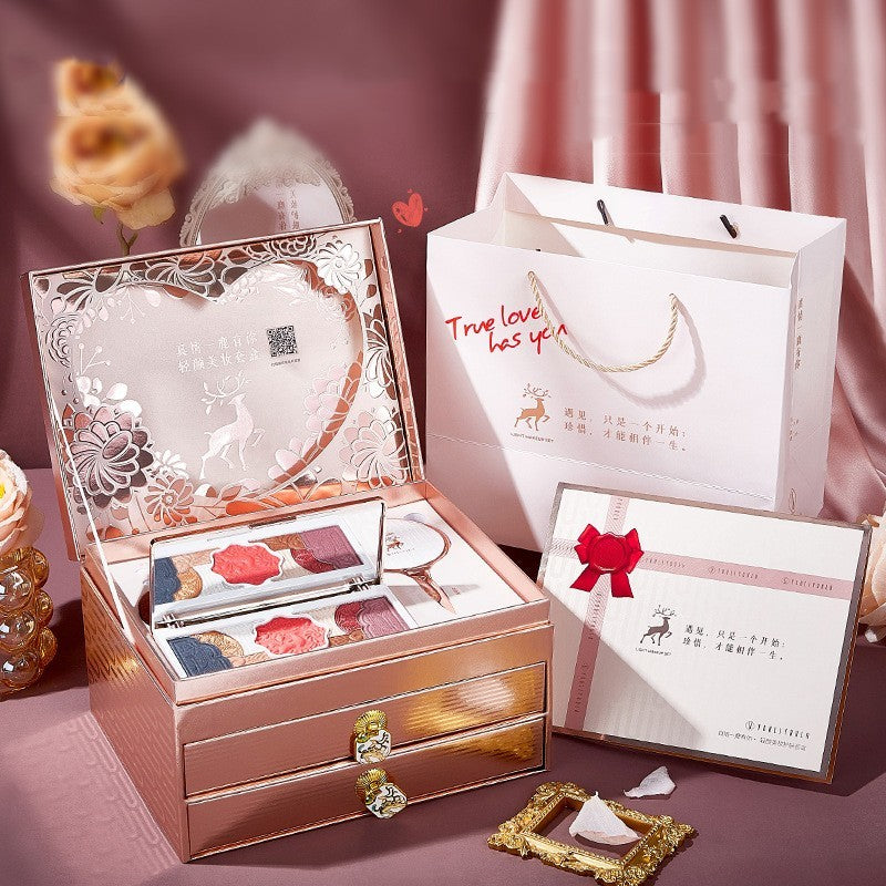 Makeup set in a decorative box with a branded gift bag and card on a pink background