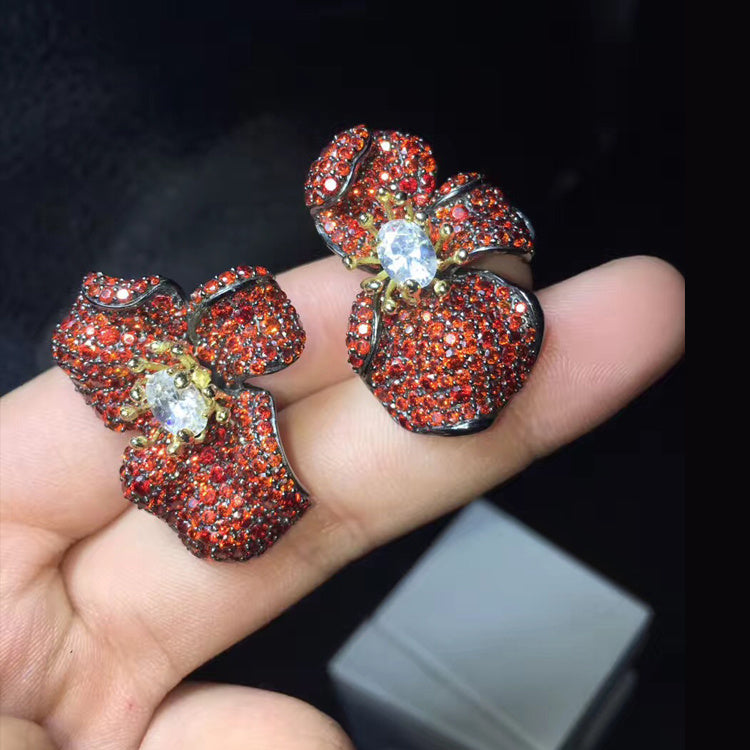 Red gemstone earrings held in a hand with a dark background