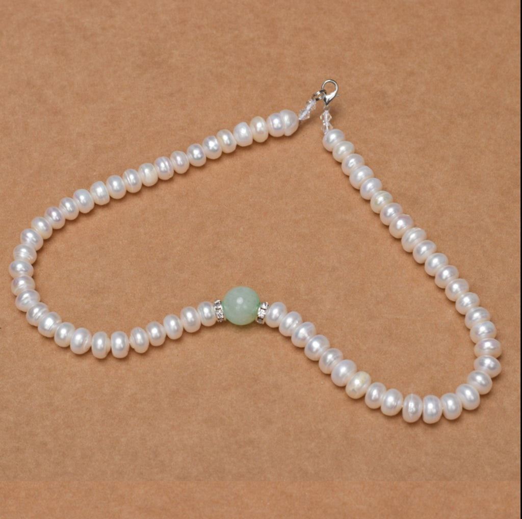 Pearl necklace with a green bead on a brown background