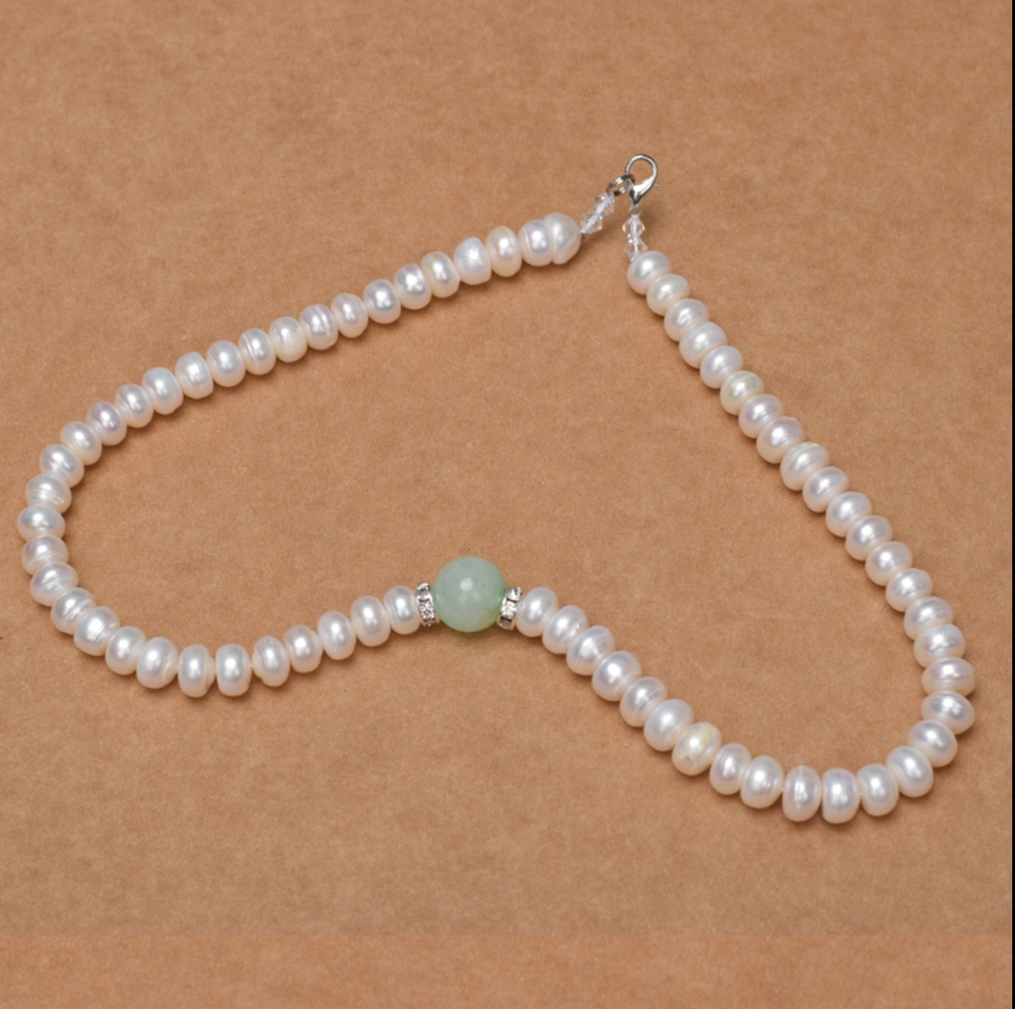 Pearl necklace with a green bead on a brown background