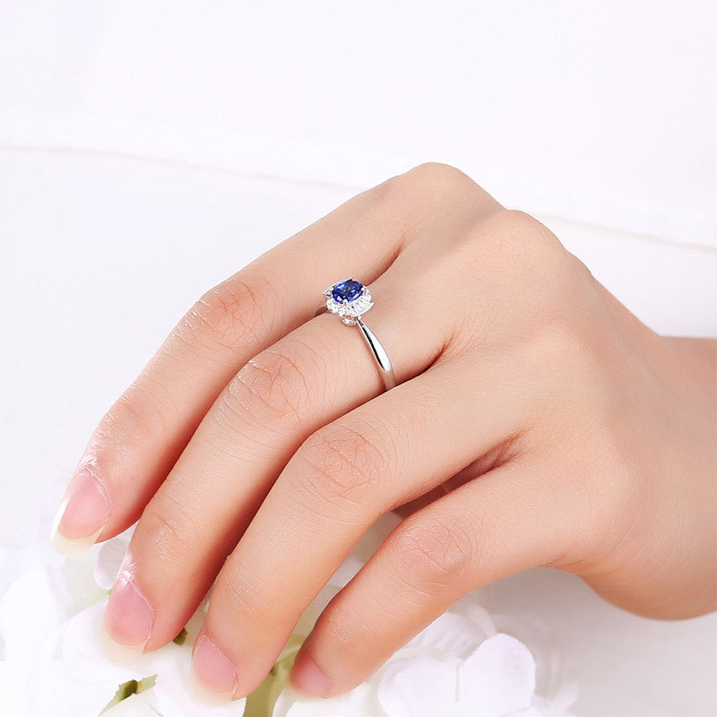 Hand wearing a silver ring with a blue gemstone on a white background