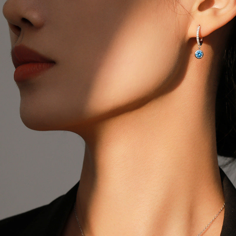 Close-up of a person wearing a blue gemstone earring against a neutral background
