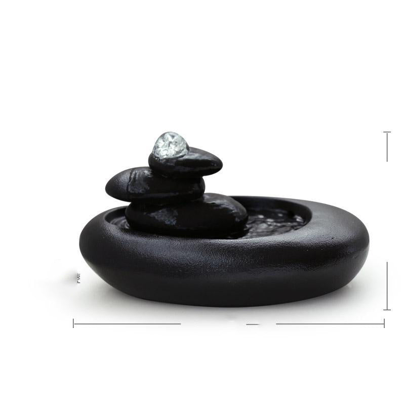 Black stone-like incense burner with a small crystal on top against a white background