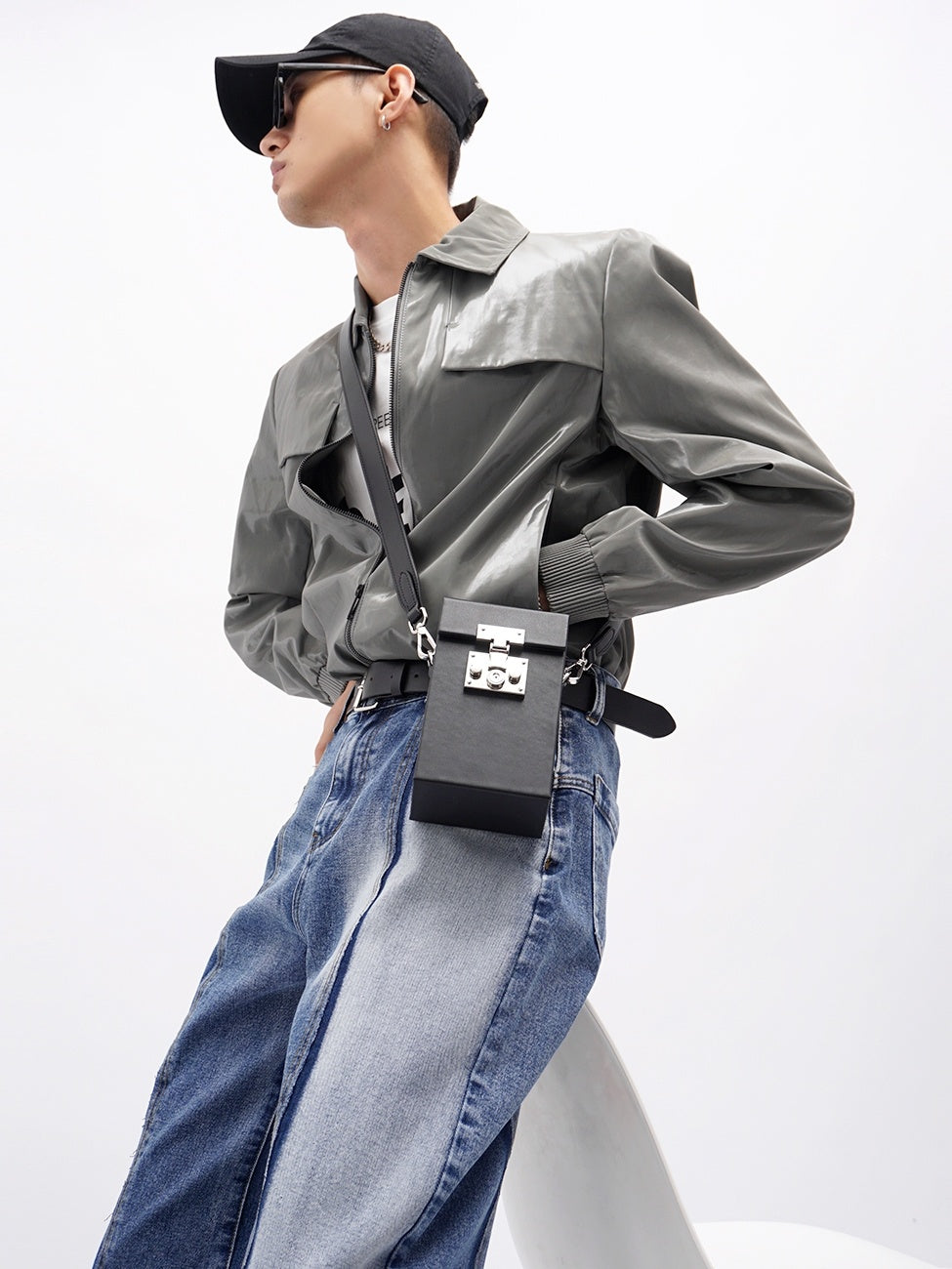 Person wearing a gray jacket, blue jeans, and black cap with a black bag on a white background