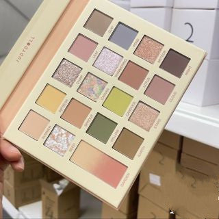 Makeup palette with various colors held by a hand, with a blurred background.