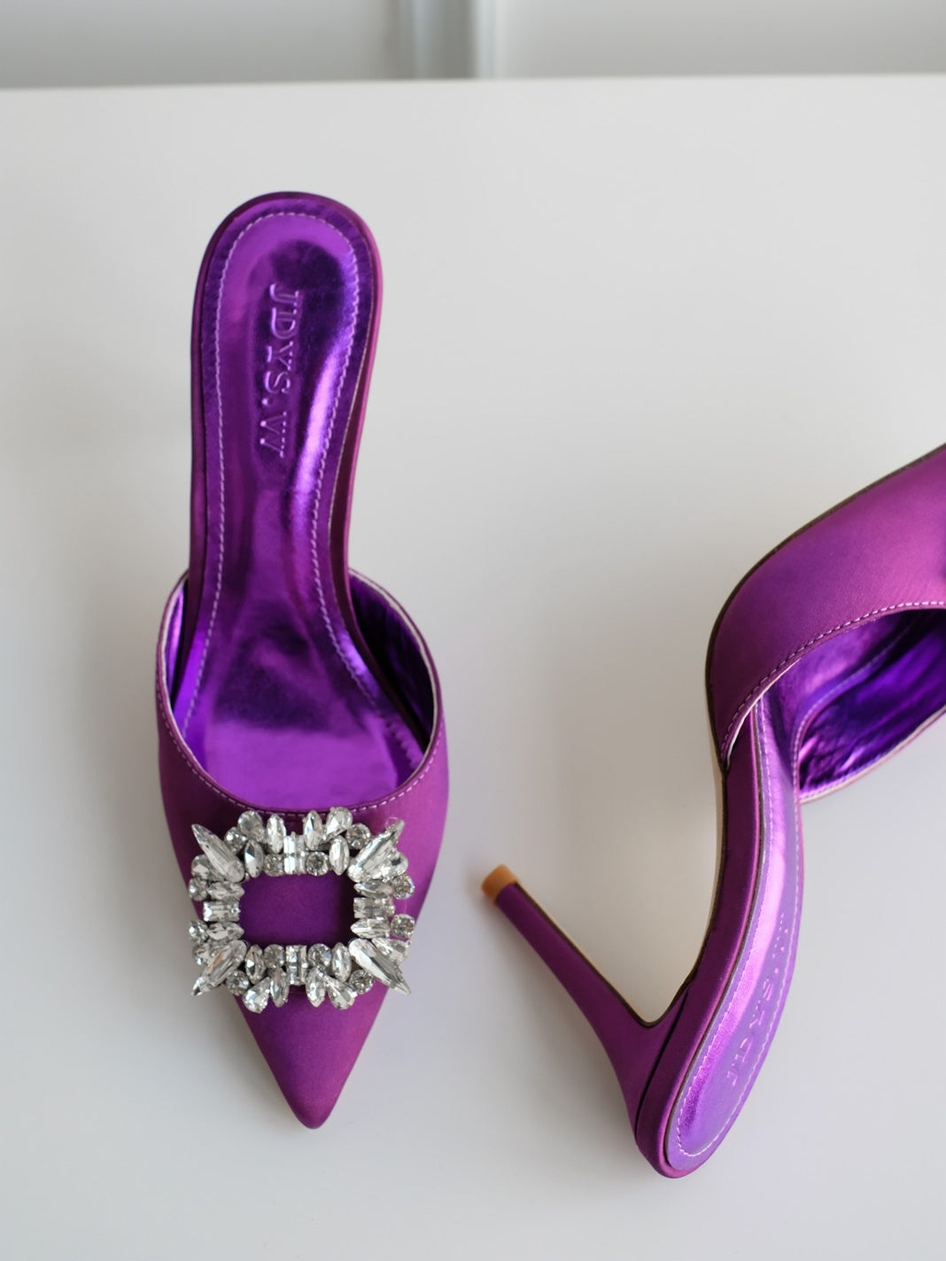 Purple high-heeled shoes with a decorative brooch on a white background