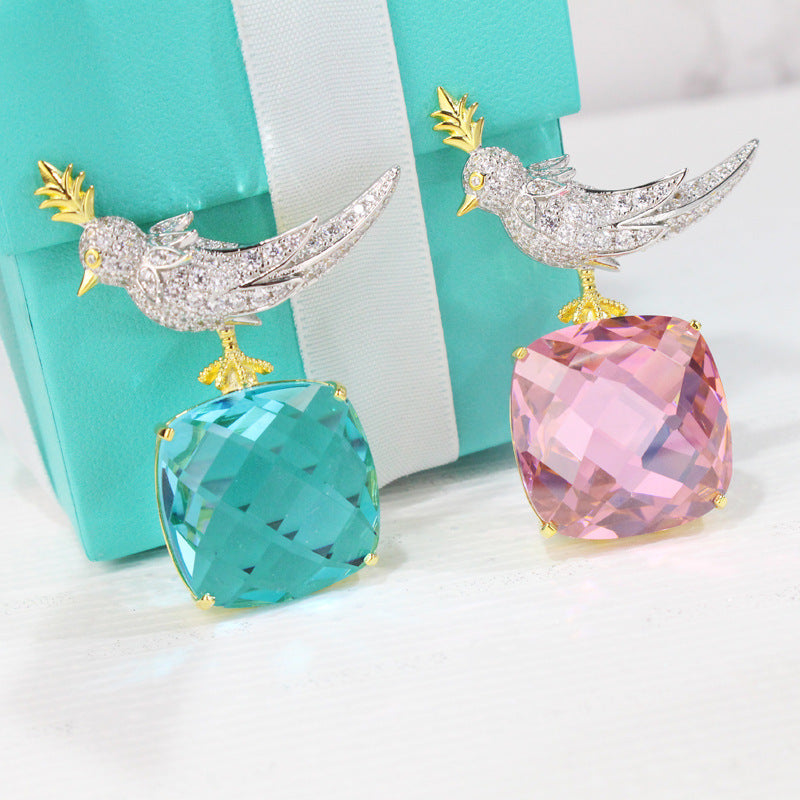 Pair of earrings with bird designs on colorful gemstones against a turquoise box background.