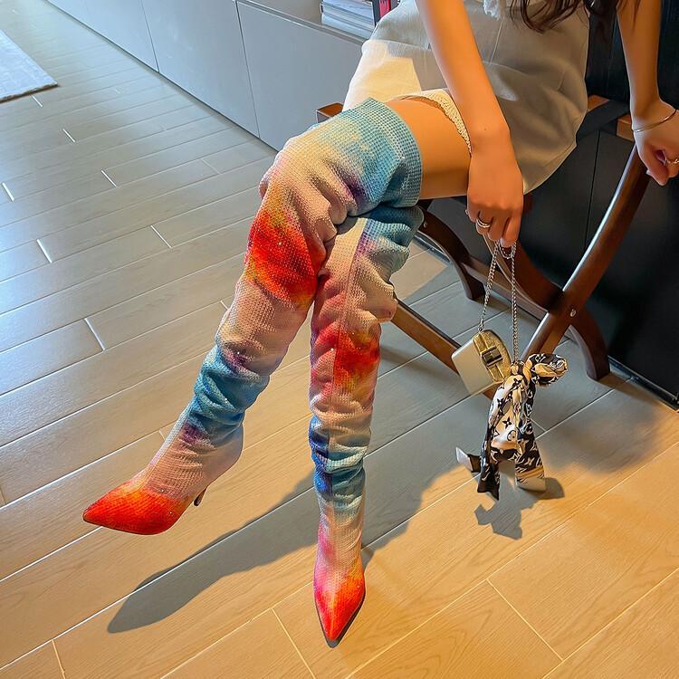 Person wearing colorful tie-dye pants and red high heels in a room with wooden flooring.