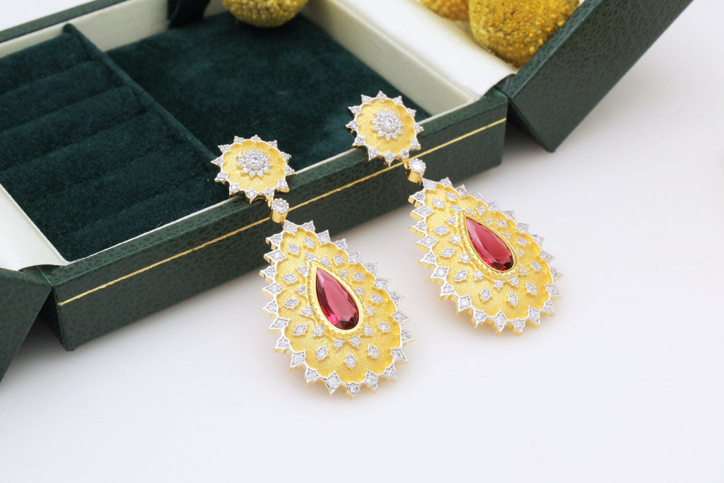 Gold earrings with red gemstones on a white surface with green jewelry box.