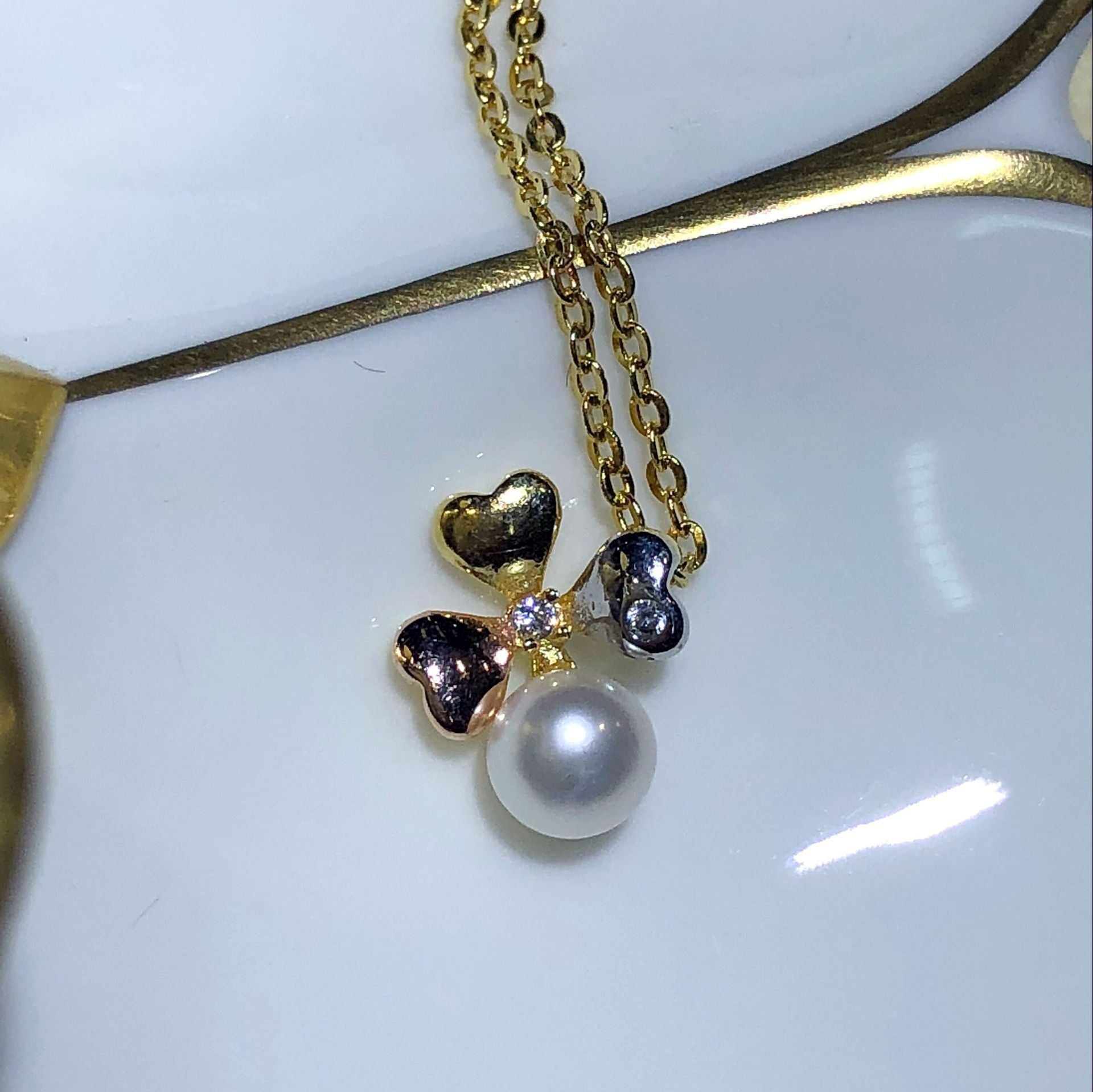 Gold necklace with a bow and pearl pendant on a white background