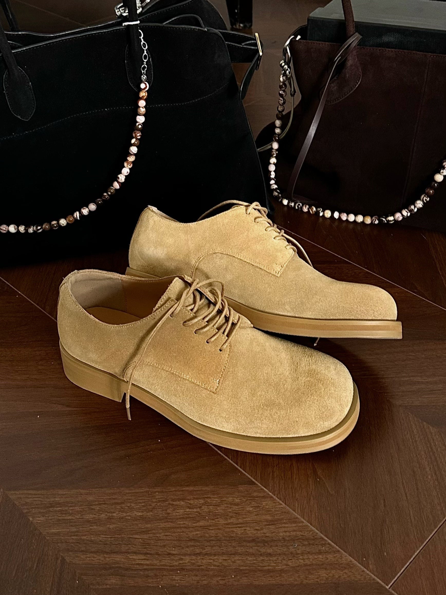 Pair of tan suede shoes on a wooden floor with a dark background