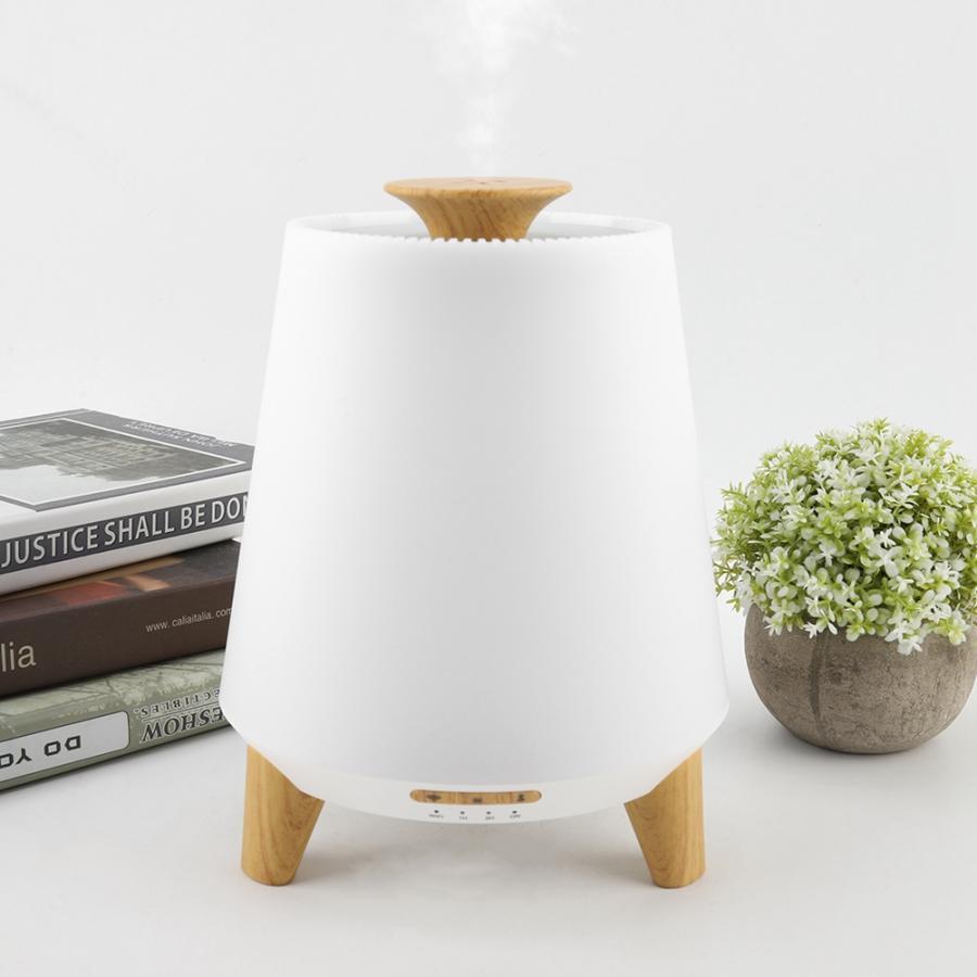 White diffuser with wooden accents on a white surface with books and a plant in the background