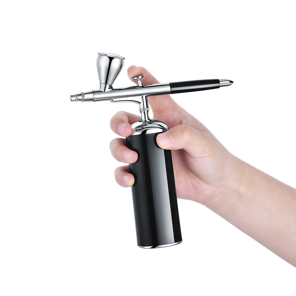 Hand holding a black and silver airbrush gun on a white background