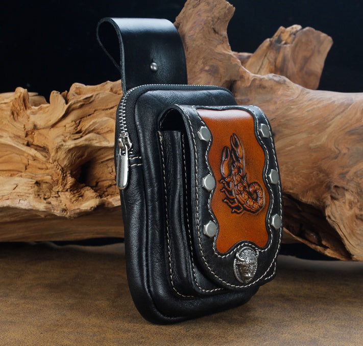 Black leather pouch with brown leather patch featuring a design, placed on wooden logs.